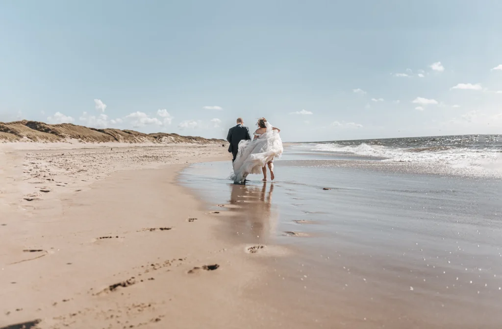 Brudepar går langs vandkanten på en sandstrand