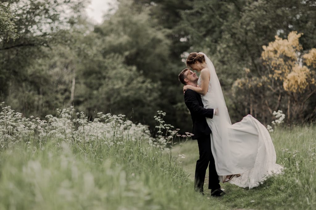 Brudgom løfter bruden i en blomstrende eng – bryllupsfotografi i naturen