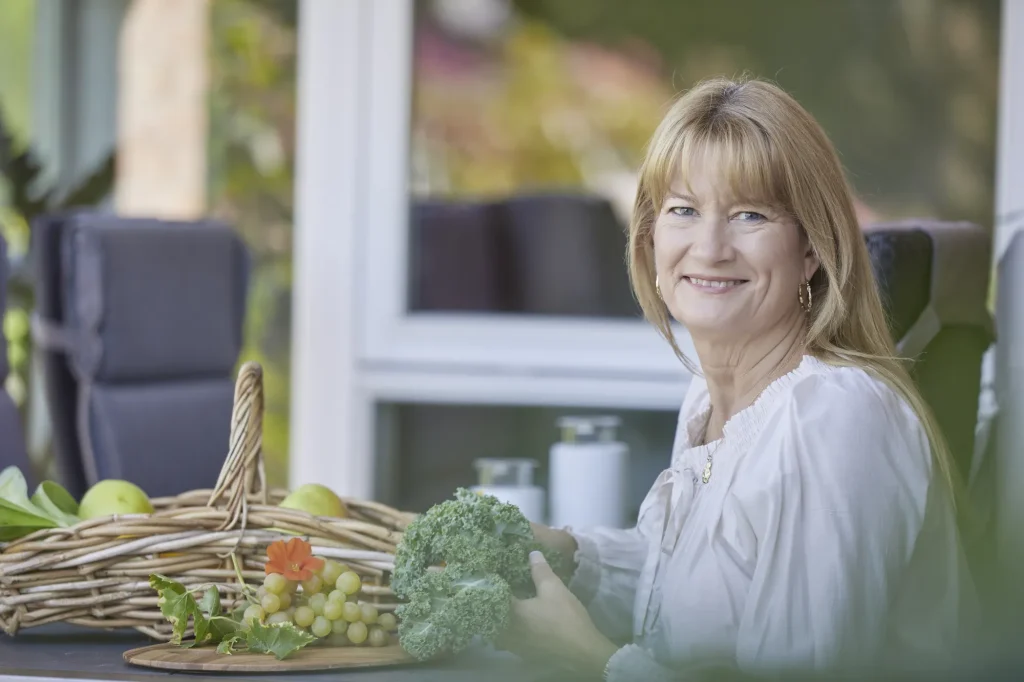 Smilende kvinde ved havebord med kurv af frugt og grøntsager