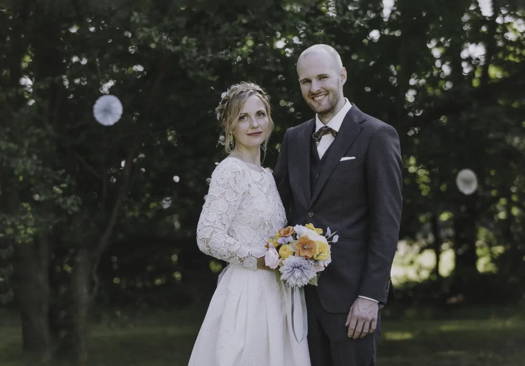 Brudepar smiler med buket foran skoven