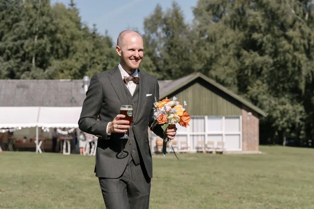 Brudgom med øl og buket foran festteltet