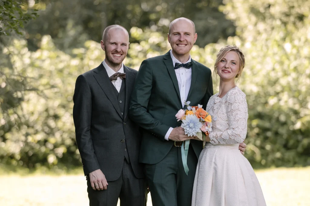 Brudepar med forlover foran grøn hæk