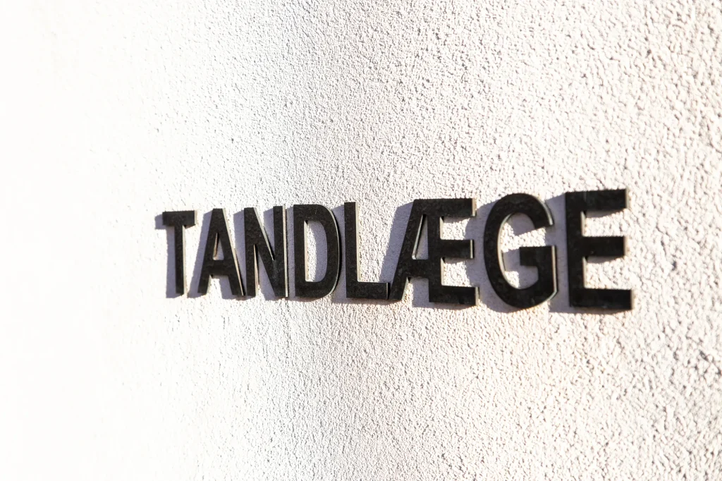 Nærbillede af TANDLÆGE-skiltet på klinikkens hvide facade