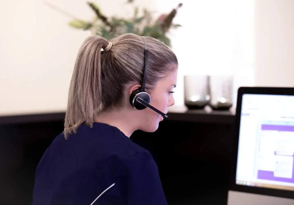 Receptionist med headset ved computer i tandklinikken