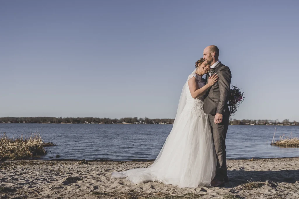 Brudepar omfavner hinanden ved søens strand