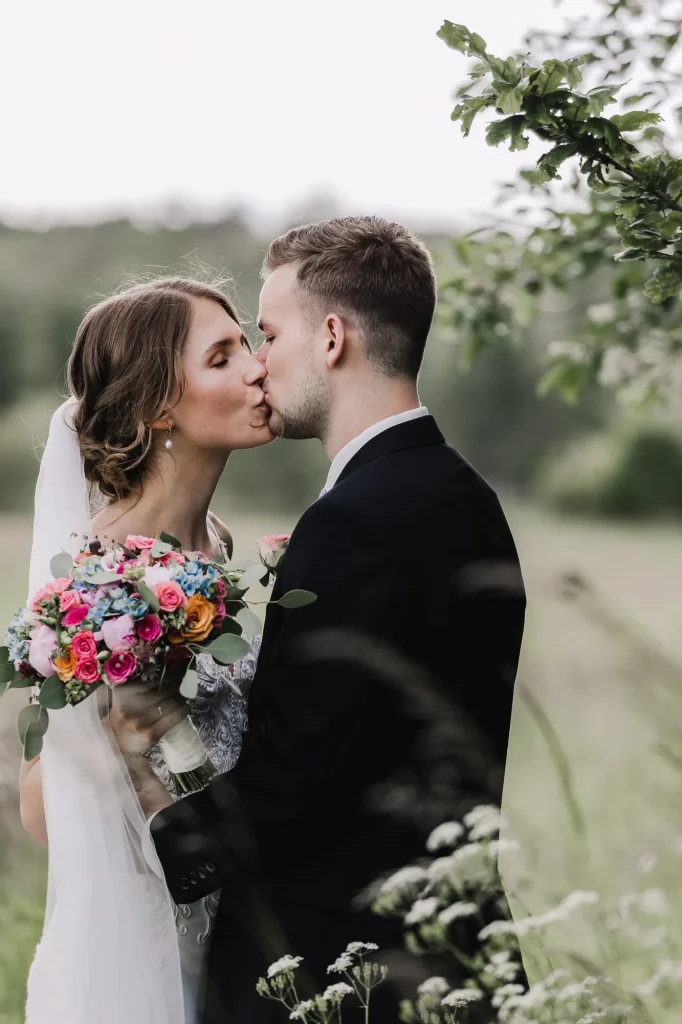 Brudepar kysser i engen med farverig brudebuket