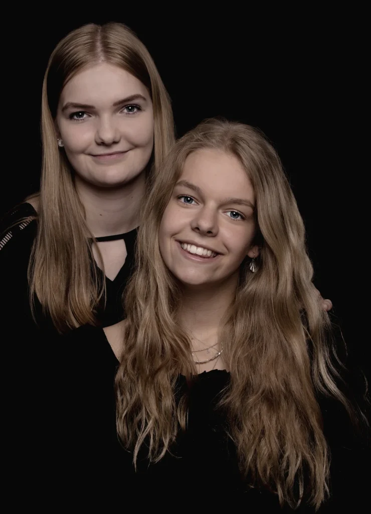 Studieportræt af to søstre med langt hår foran sort baggrund